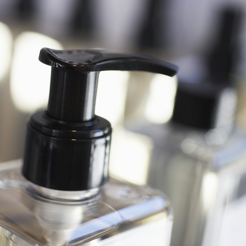 Parte superiore del dispenser di una bottiglia di sapone o lozione trasparente su uno sfondo sfocato.